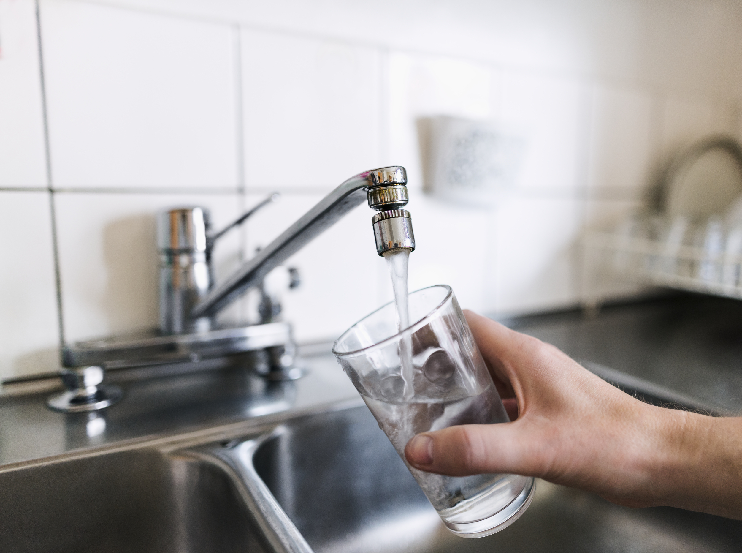 En person fyller sitt glas med vatten under en rinnande kökskran